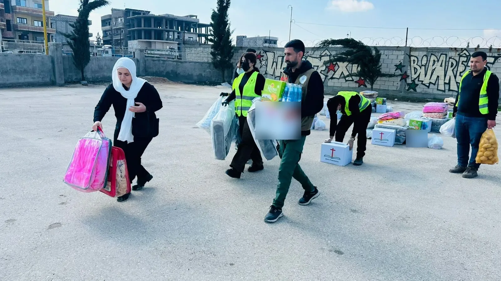 Mensen dragen hulppakketten over een plein tijdens de uitdeling in Noordoost-Syri&euml;, maart 2026